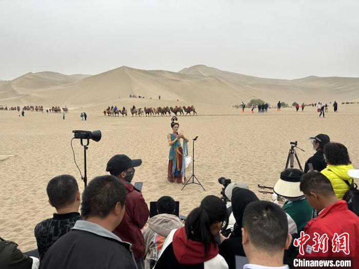 圖為2023年4月底，敦煌大漠“逐舞者”奧楠在鳴沙山月牙泉景區(qū)視頻直播，吸引游人圍觀?！●T志軍 攝